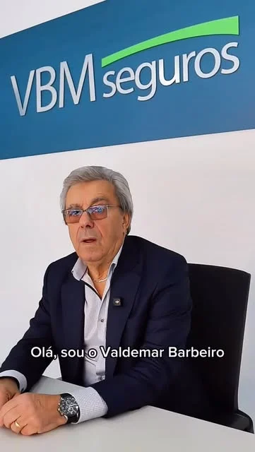 Valdemar Barbeiro, sentado a uma secretária, à frente de um painel com o logótipo VBM seguros